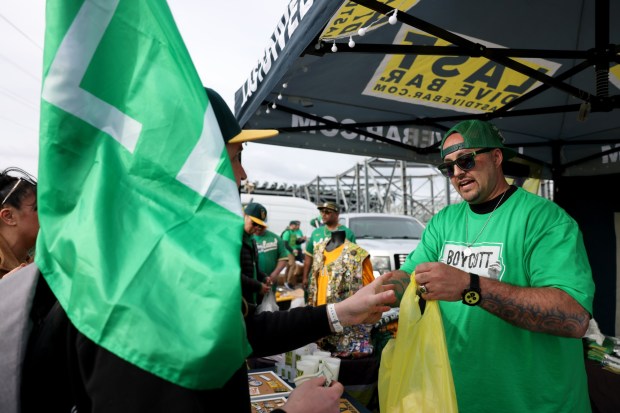 Bryan Johansen, right, founder of A's fan group Last Dive Bar, sells merchandise during a boycott opening day block party in the parking lot before their MLB opening day game against the Cleveland Guardians at the Coliseum in Oakland, Calif., on Thursday, March 28, 2024. (Ray Chavez/Bay Area News Group)