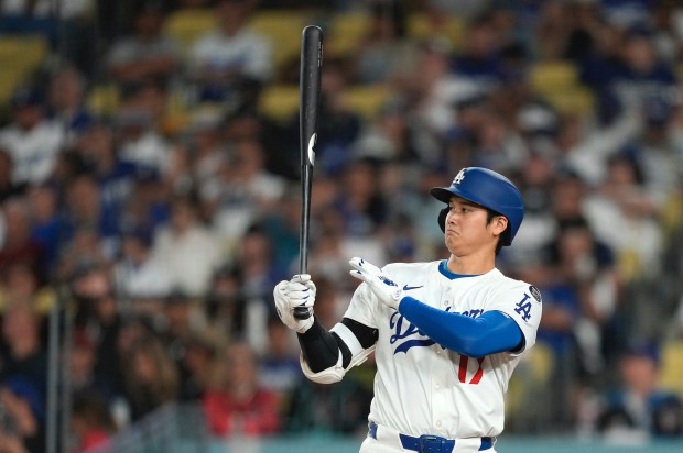 Dodgers star Shohei Ohtani brushes away an insect as he...