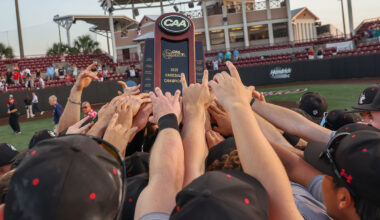 Mens baseball players stand in a huddle with their hands raised.