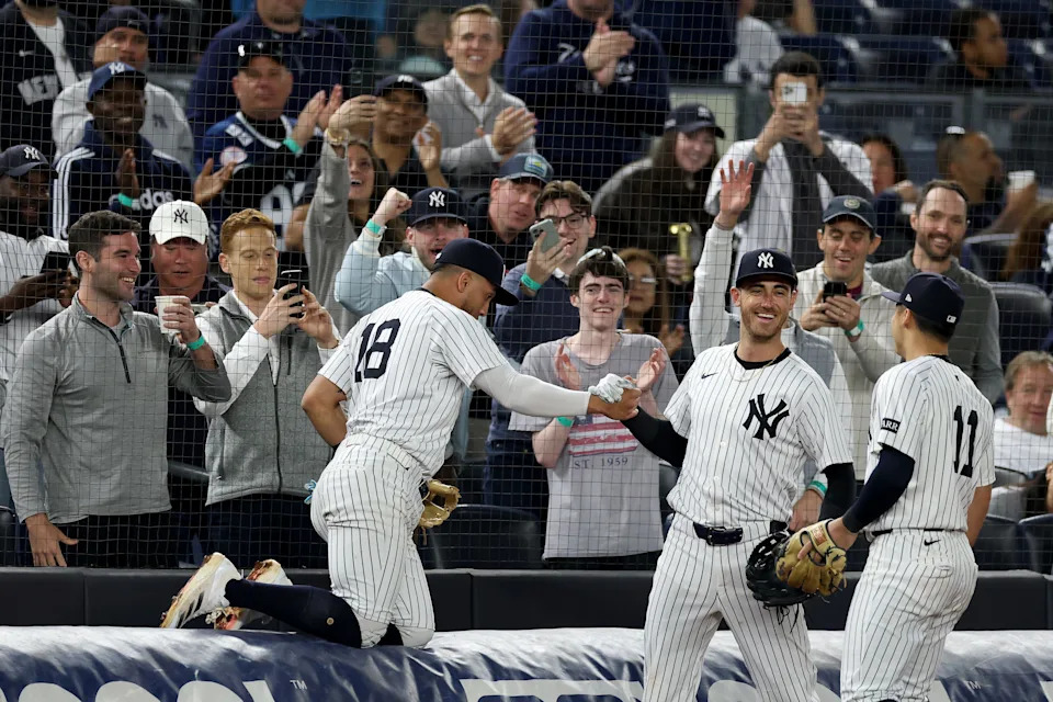 NEW YORK, NEW YORK - MAY 20: Oswald Peraza #18 of the New York Yankees is helped up by Cody Bellinger #35 after falling over a tarp while catching a foul ball against the Texas Rangers during the sixth inning at Yankee Stadium on May 20, 2025 in New York City.