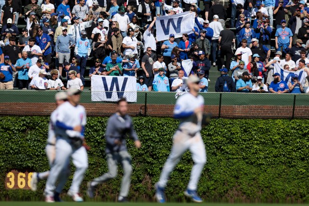 Chicago Cubs fans in the bleachers cheer and hold up "W" flags as the outfielders trot toward their teammates after the Chicago Cubs defeated the Chicago White Sox 6-2 at Wrigley Field on Sunday, May 18, 2025. (Eileen T. Meslar/Chicago Tribune)
