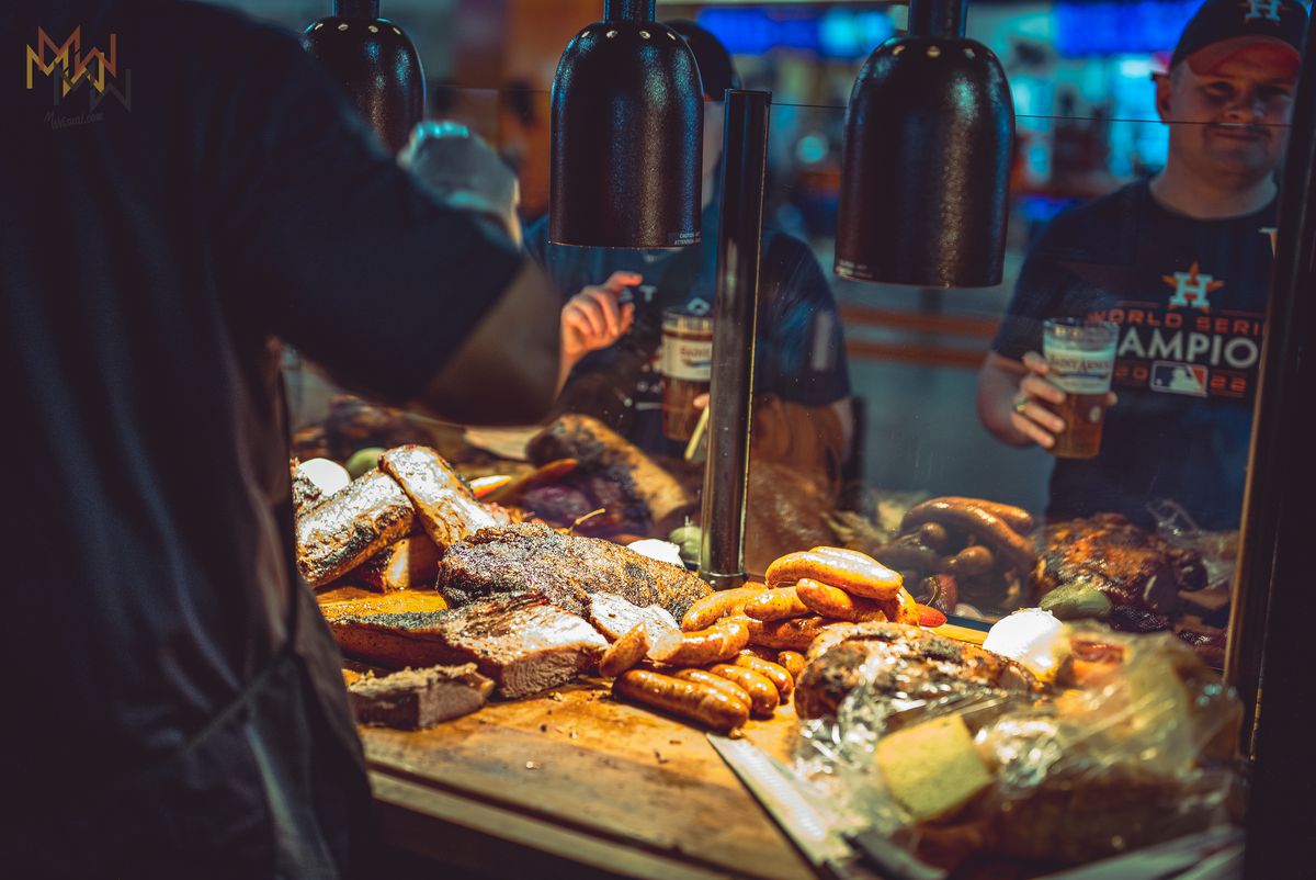 the Butcher’s vendor displays brisket, sausage, turkey, and other meats under a heat lamp at Daikin Park.