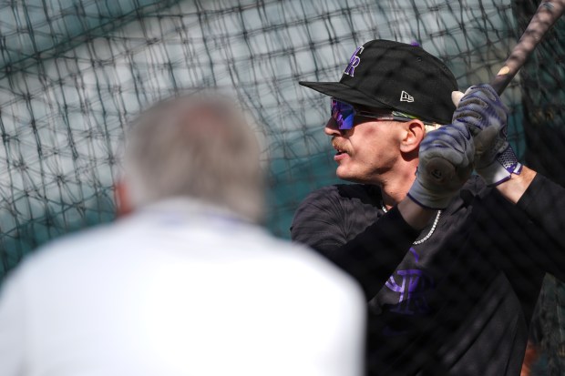 Colorado Rockies' Zac Veen, back, warms up in the batting cage as general manager Bill Schmidt looks on before a baseball game against the Milwaukee Brewers Wednesday, April 9, 2025, in Denver. (AP Photo/David Zalubowski)