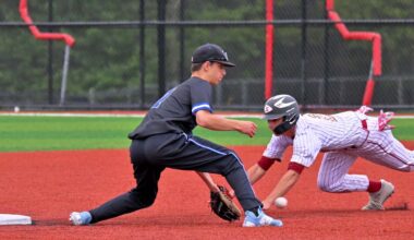 A baseball runner wearing red and white striped uniform slides into second base as the fielder in black uniform makes the catch and the out