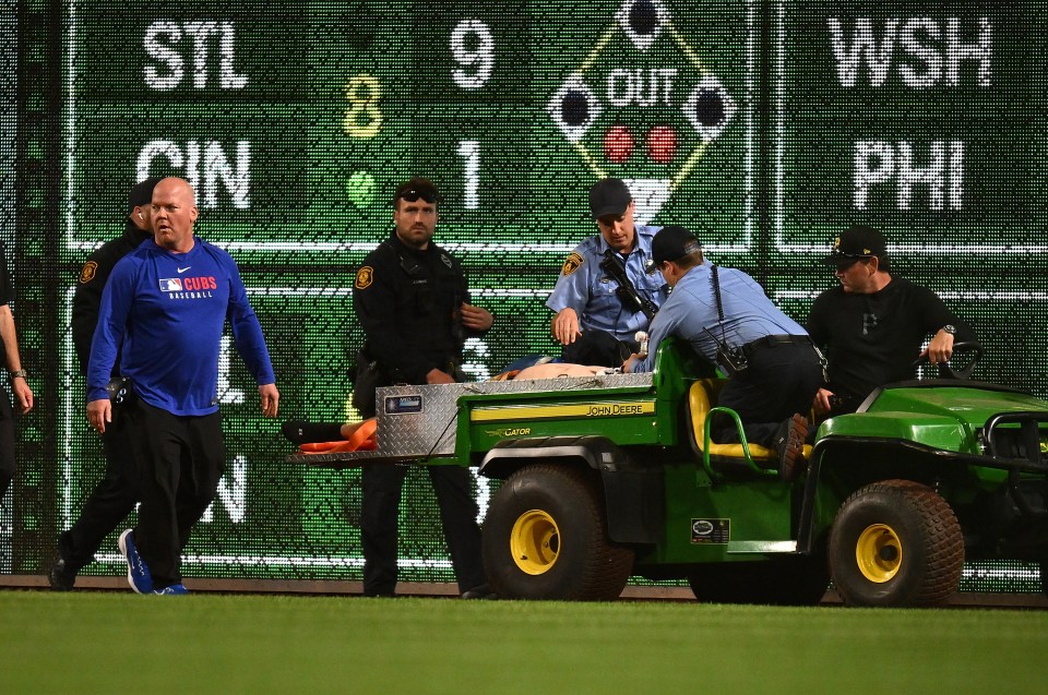Fan being carted off baseball field on a utility vehicle.