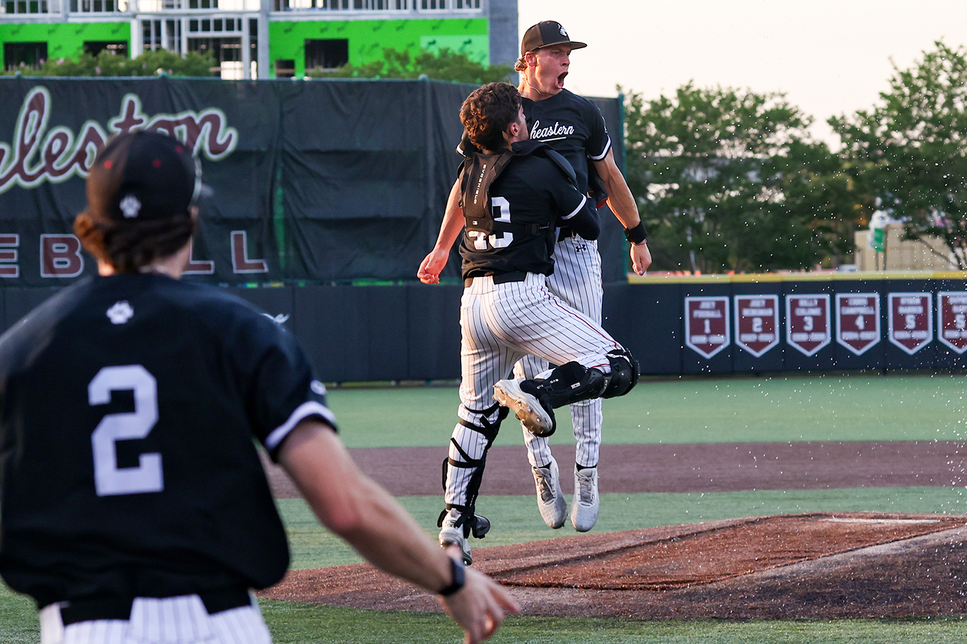 Northeastern mens baseball players jump in celebration on the pitch. 