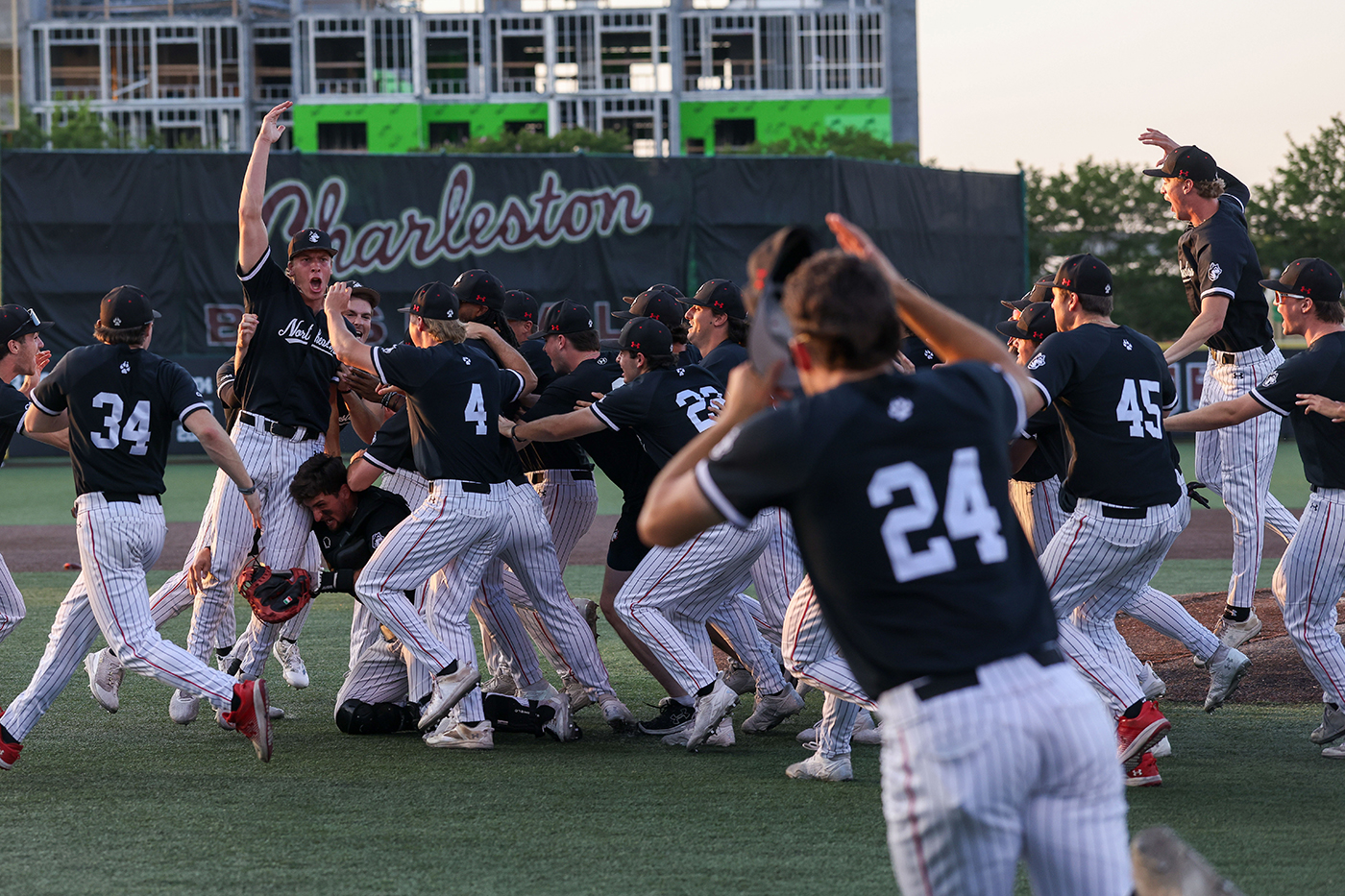 Northeastern mens baseball players jump in celebration on the pitch. 