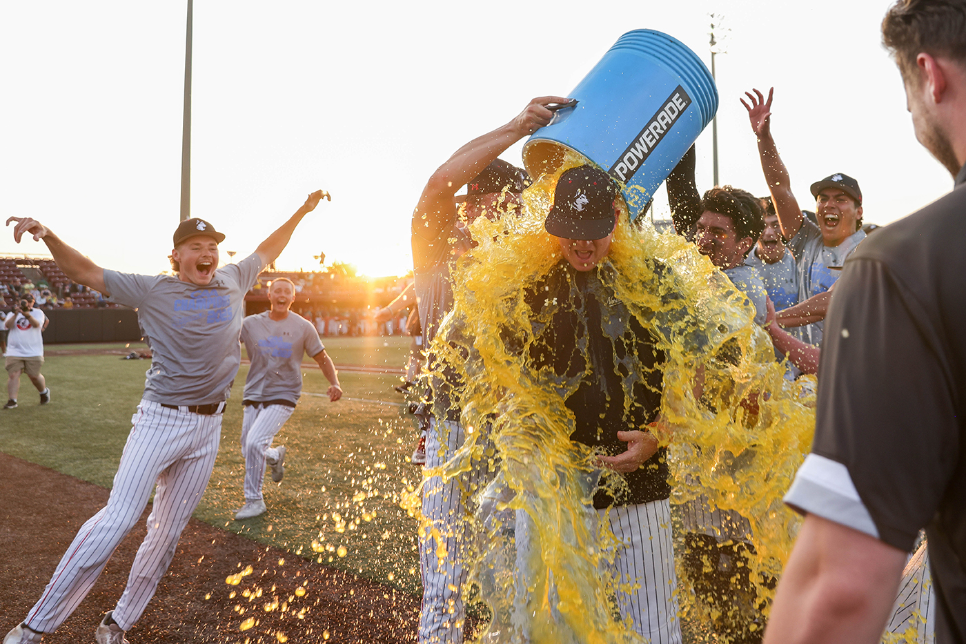 Northeastern baseball players dump a bucket of yellow powerade on their coach.