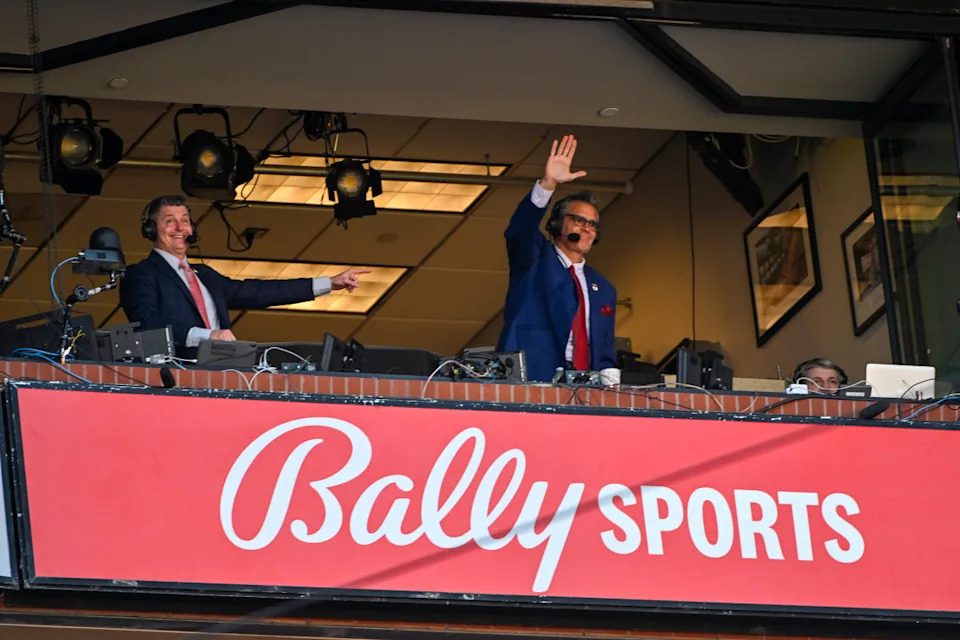 Mar 30, 2023; St. Louis, Missouri, USA; Bally Sports Midwest announcer Chip Caray and Brad Thompson wave to the fans during the second inning of an opening day game between the St. Louis Cardinals and the Toronto Blue Jays at Busch Stadium. Mandatory Credit: Jeff Curry-Imagn Images© Jeff Curry-Imagn Images