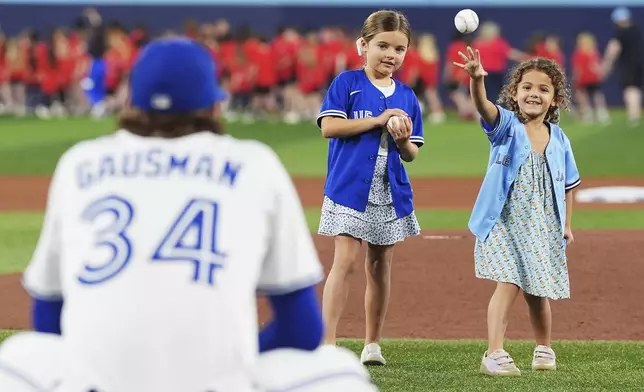 Toronto Blue Jays pitcher Kevin Gausman (34) catches the ceremonial first pitch from his daughters Sutton, right, and Sadie prior to the first inning of a baseball game against the Arizona Diamondbacks in Toronto, Wednesday, June 18, 2025. (Frank Gunn/The Canadian Press via AP)