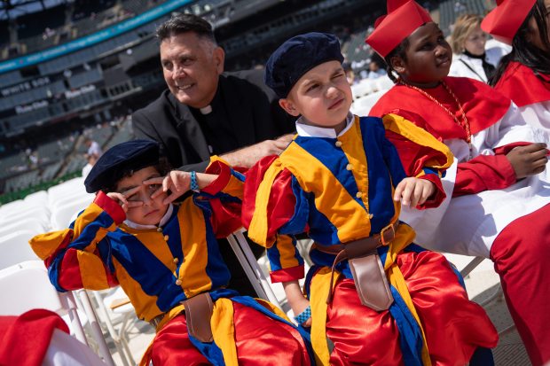 Members of Our Lady of Mount Carmel Academy Luciano Vargas, 5, and David Foerster, 5, sit in the sun before programming begins during a celebration of the election of Pope Leo XIV with a citywide gathering and Catholic Mass at Rate Field on June 14, 2025. (Audrey Richardson/Chicago Tribune)