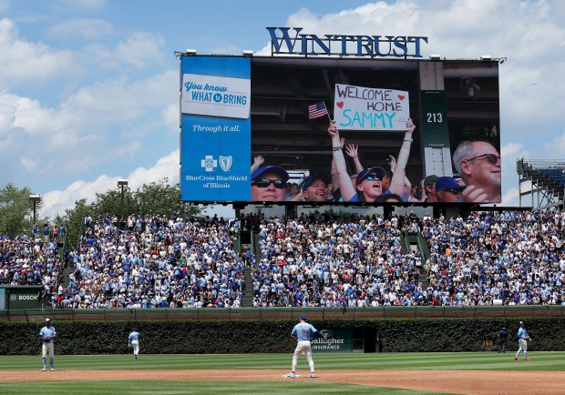 Cubs players warm up for the third inning as fans react to former Cubs slugger Sammy Sosa waving to the crowd from a suite while being honored during a game against the Mariners on June 20, 2025, at Wrigley Field. (Chris Sweda/Chicago Tribune)