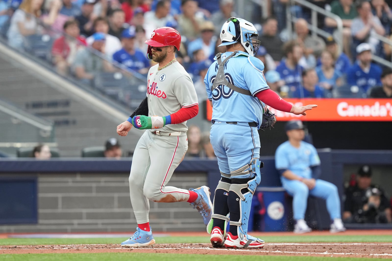 Philadelphia Phillies' Bryce Harper (3) crosses home plate in front of Toronto Blue Jays catcher Alejandro Kirk (30) after scoring off a throwing error from Blue Jays' Addison Barger during the second inning of a baseball game in Toronto, Tuesday June 3, 2025. (Chris Young/The Canadian Press via AP)