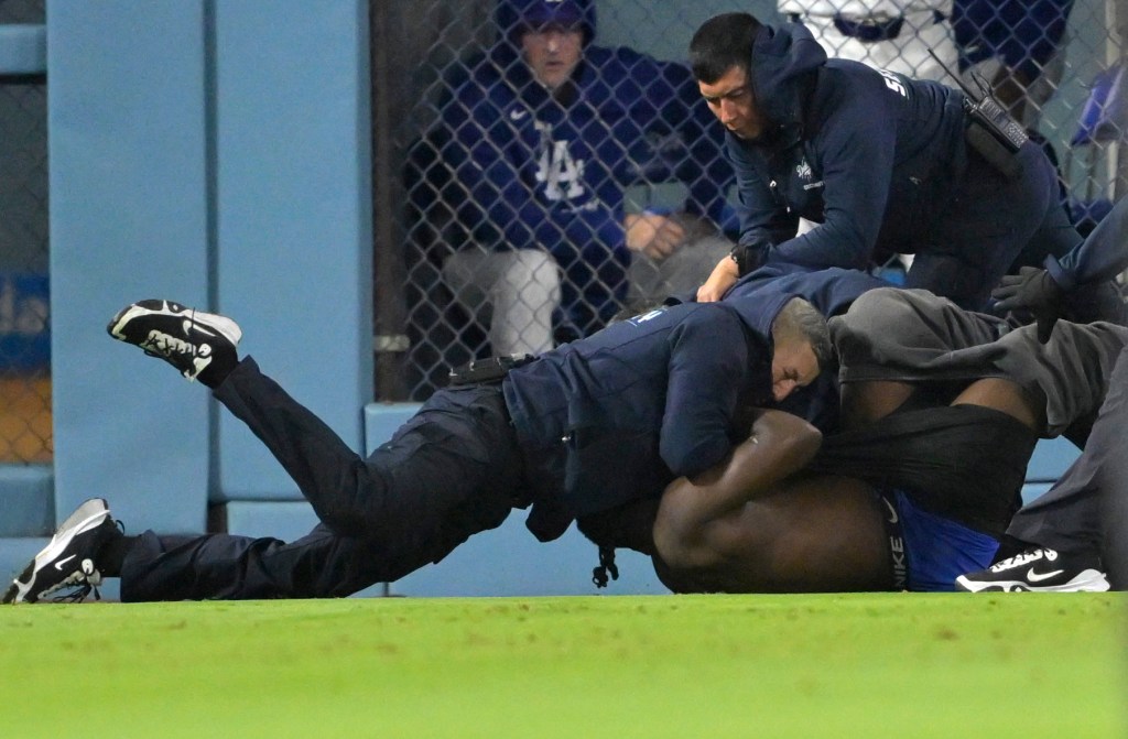 Security guards tackling a fan who ran onto the field during a baseball game.