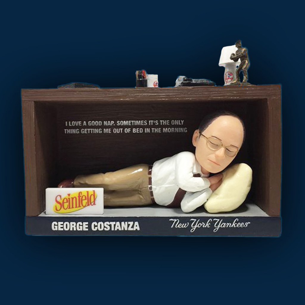 George Costanza bobblehead sleeping under a desk.