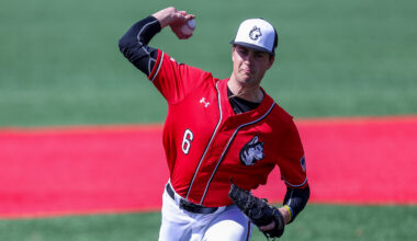 Cam Schlitter wearing a red and white Northeastern baseball uniform throwing a pitch on the baseball field.