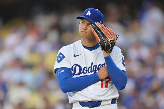 Dodgers starting pitcher Shohei Ohtani listens to the PitchCom device...
