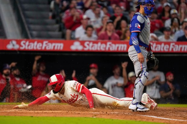 The Angels’ Jo Adell, left, scores as Texas Rangers catcher...