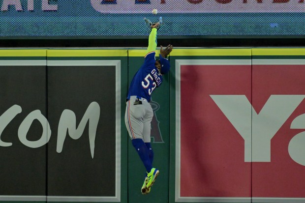 Texas Rangers right fielder Adolis Garcia reaches over the wall...
