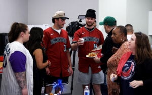 A group of people, including two in red "Diamondbacks" jerseys, gather in a casual indoor setting.