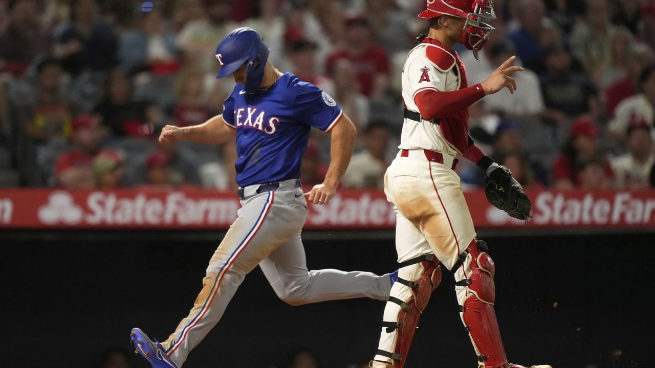 Texas Rangers' Wyatt Langford, left, scores on a single by Evan Carter as Los Angeles Angels catcher Logan O'Hoppe stands by during the eighth inning of a baseball game Wednesday, July 30, 2025, in Anaheim, Calif. (AP Photo/Mark J. Terrill)