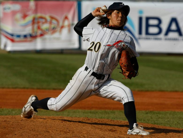 Young Japanese woman wearing a baseball uniform throws a pitch from a mound.