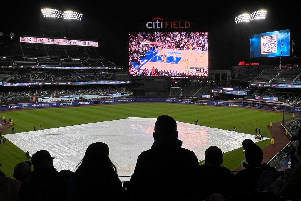 Fans at Citi Field watching a basketball game on the scoreboard during a rain delay.