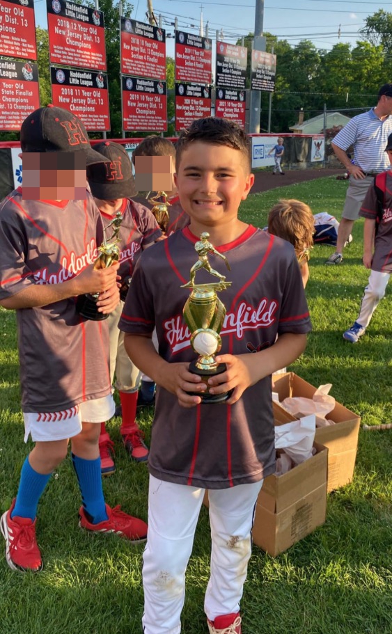 Boy in baseball uniform holding a trophy.