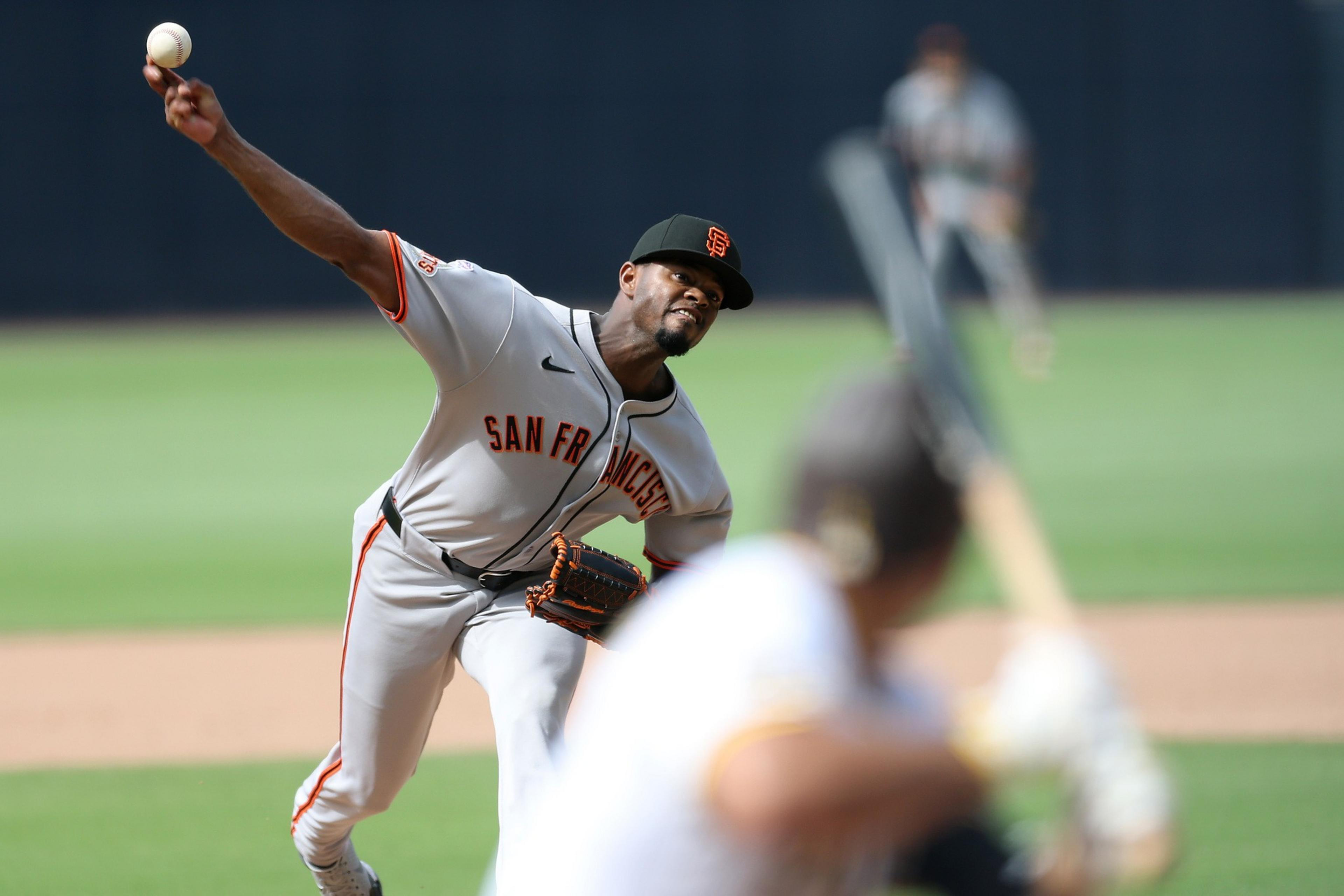 A San Francisco Giants pitcher throws a baseball towards a batter, captured mid-throw during a game on a green field.