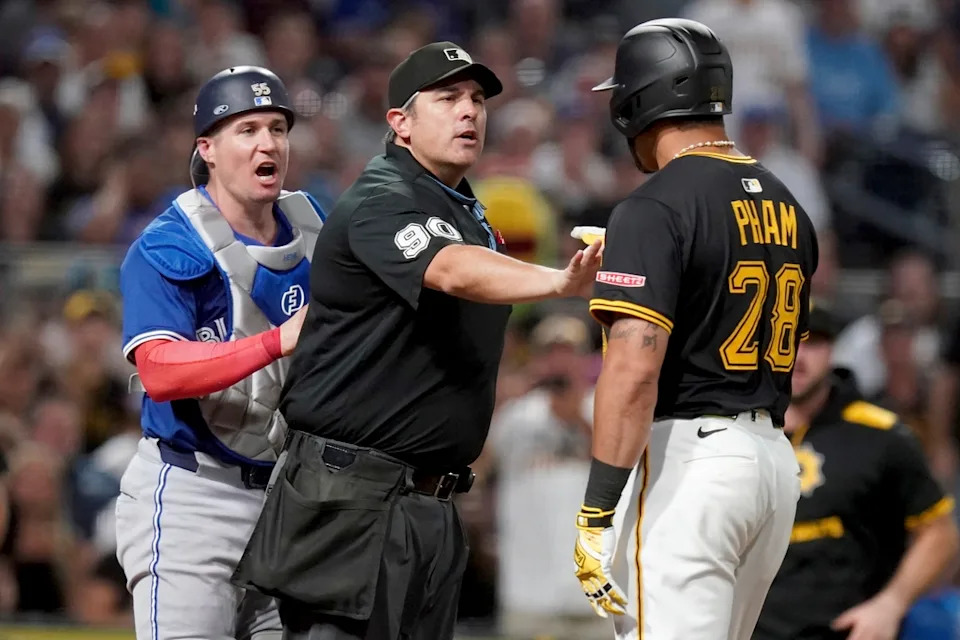  Home plate umpire Mark Ripperger, center, gets between Toronto Blue Jays catcher Tyler Heineman, left, and Pittsburgh Pirates’ Tommy Pham, right, during the seventh inning of a baseball game Monday, Aug. 18, 2025, in Pittsburgh. (AP Photo/Matt Freed)