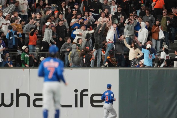 Cubs shortstop Dansby Swanson, foreground, and left fielder Ian Happ (8) watch as fans reach for a two-run home run hit by the Giants' Matt Chapman during the sixth inning on Aug. 26, 2025. (AP Photo/Jeff Chiu)