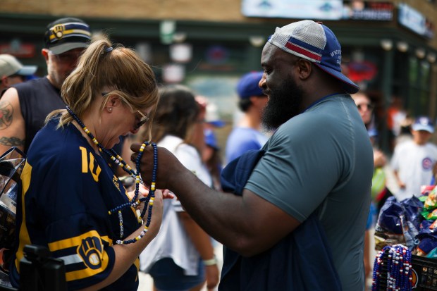 Marcus Lyons, a vendor of 36 years, puts Milwaukee Brewers beads on Kari McBride, of Milwaukee, outside Wrigley Field before the Chicago Cubs game against the Milwaukee Brewers on Monday, Aug. 18, 2025. (Eileen T. Meslar/Chicago Tribune)