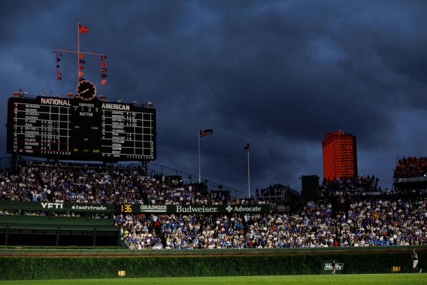 The sun sets on a building and part of the flags above the scoreboard while the Chicago Cubs play the Milwaukee Brewers during the third inning at Wrigley Field on Wednesday, Aug. 20, 2025, in Chicago. (Armando L. Sanchez/Chicago Tribune)