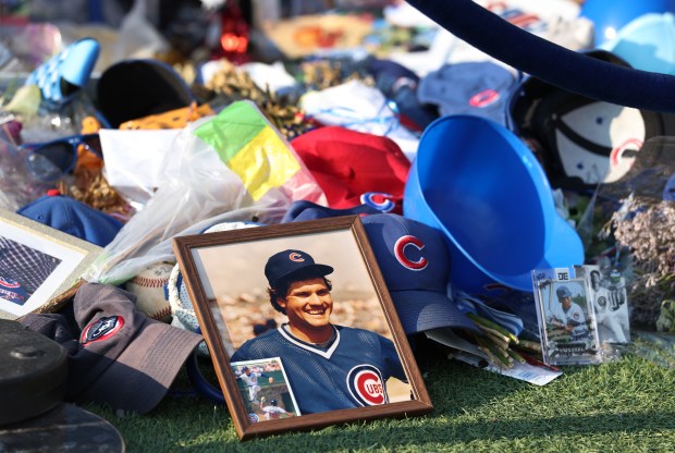 A photo of a young Ryne Sandberg is seen among items honoring the Cubs legend at the base of his statue in Gallagher Way outside of Wrigley Field in Chicago before a game between the Cubs and the Cincinnati Reds at Wrigley Field in Chicago on Aug. 5, 2025. Sandberg died last week after a battle with cancer. (Chris Sweda/Chicago Tribune)