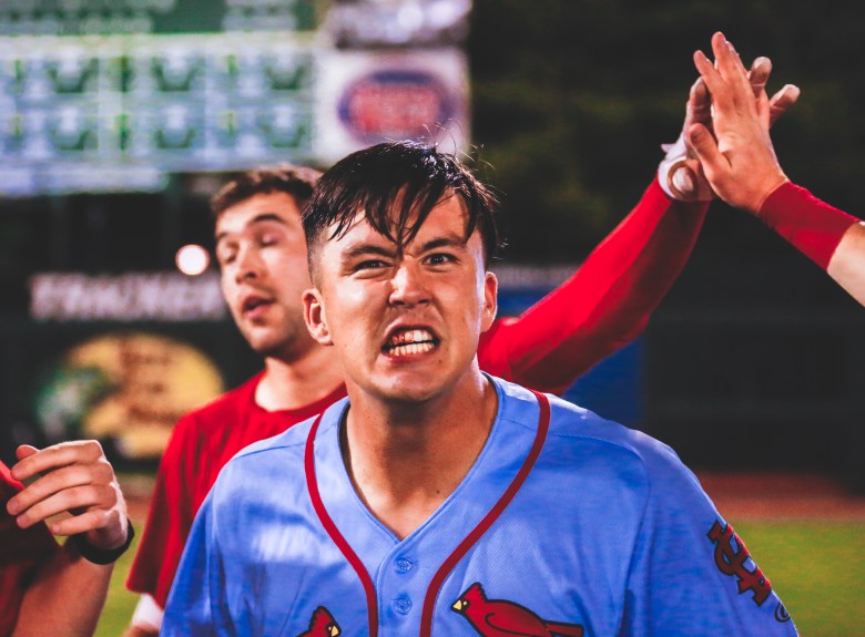 A man in a blue baseball jersey looks at the camera. He has blood on some of his teeth