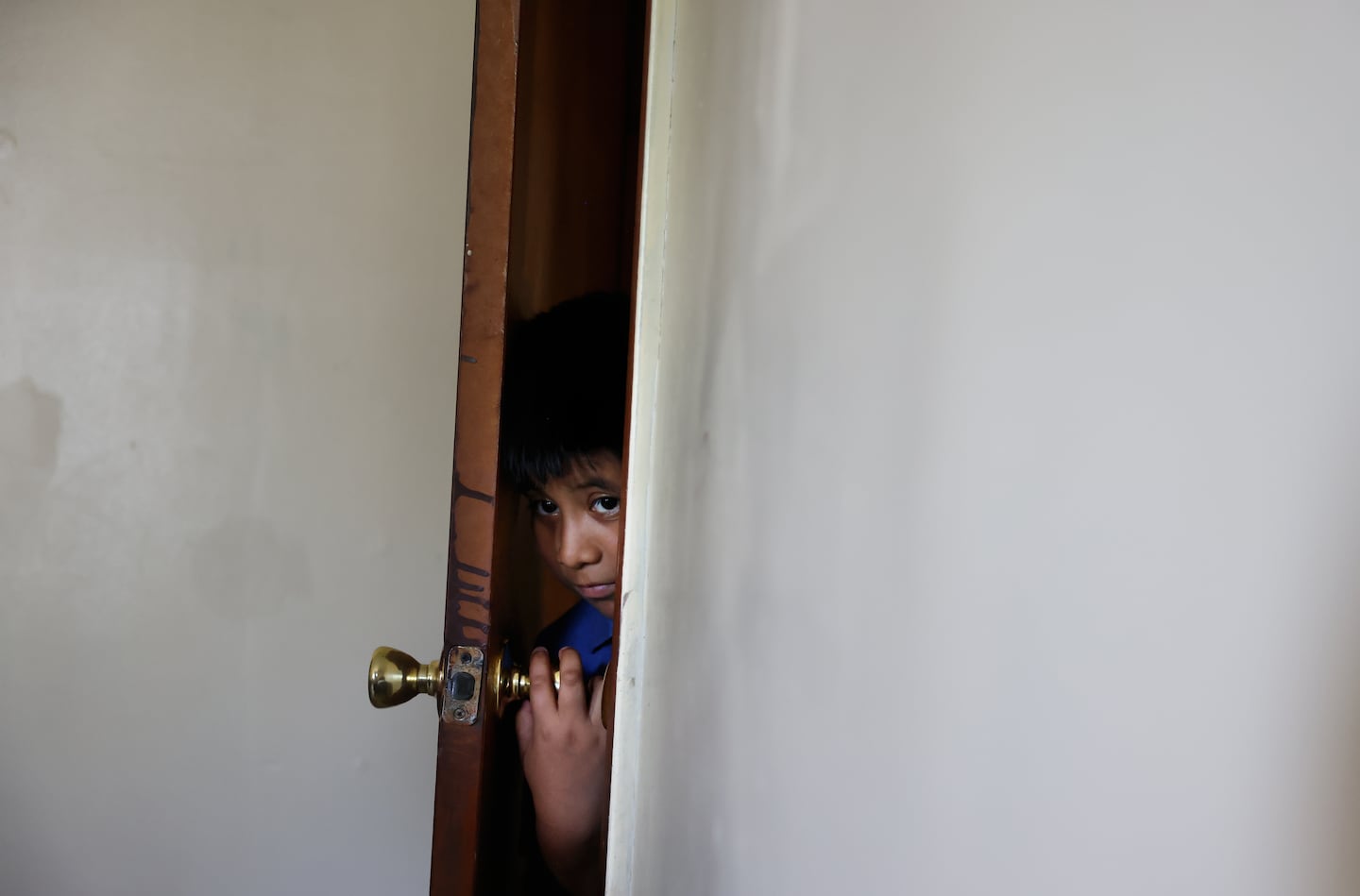Ery Perez Gutierrez, 9, peered through the door into the living room of his family’s apartment in Springfield on July 15. Ery participated in a summer program last year, but since President Trump froze education funds for the Migration Education Program, a grant that supports children of agricultural and fishery workers, he has had to stay home instead. 