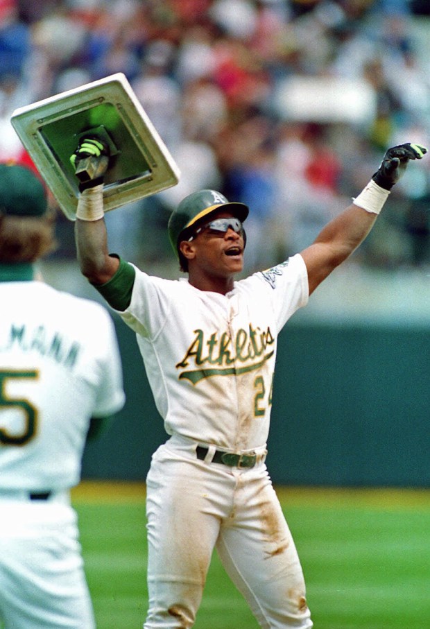 Oakland Athletics' Rickey Henderson holds up third base after breaking Lou Brock's all-time career record for stolen bases during the fourth inning of a baseball game against the New York Yankees in Oakland, Calif. It was his 939th career stolen base. (AP Photo/Alan Greth)