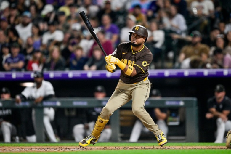 A man in a brown San Diego Padres uniform swings the bat from the left side with fans visible behind him.