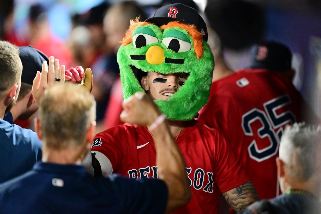 Jarren Duran celebrates a two-run home run with teammates in the dugout while wearing a green furry monster hat.