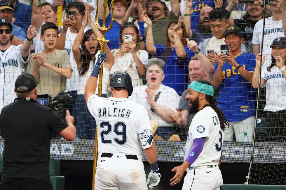 Seattle Mariners' J.P. Crawford, right, looks on as Cal Raleigh (29) lifts the trident after...