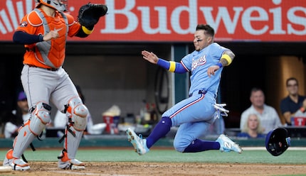 The Texas Rangers' Cody Freeman slides into home plate ahead of the throw to Houston Astros...