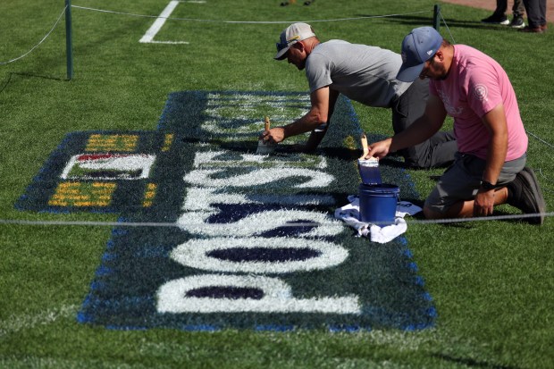 Workers paint a playoff logo on the grass at Wrigley Field on Monday, Sept. 29, 2025, as the team gets ready to face the Padres in a wild-card playoff series starting on Tuesday. (Terrence Antonio James/Chicago Tribune)