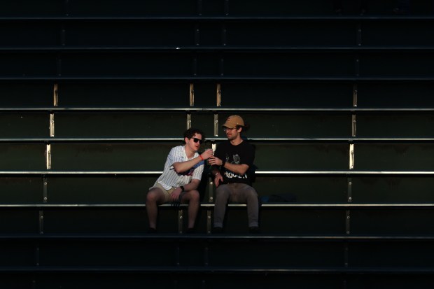Two fans share a beer as the setting sun casts a sliver of light in the right-field bleachers before a Cubs-Mets game at Wrigley Field on Sept. 25, 2025, in Chicago. (John J. Kim/Chicago Tribune)