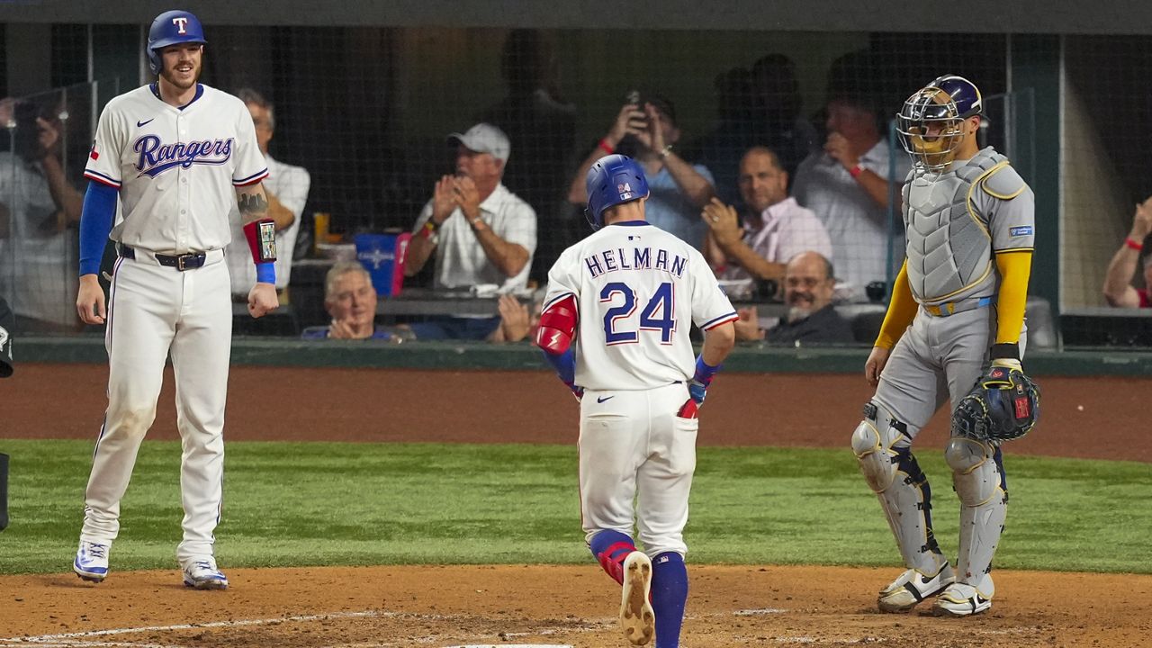 Texas Rangers' Michael Helman (24) prepares to cross home after hitting a two-run home run to score Jonah Heim, left, as Milwaukee Brewers catcher William Contreras, right, looks on during the fifth inning of a baseball game Tuesday, Sept. 9, 2025, in Arlington, Texas. (AP Photo/Julio Cortez)