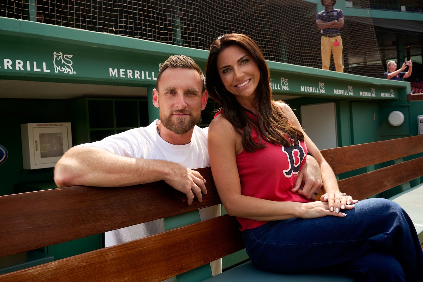 The couple poses in a dugout at Fenway. Jenny Dell is on the right sitting on a bench and wearing a red Boston Red Sox T-shirt. Will Middlebrooks is standing behind the bench on the left with his right arm around her.