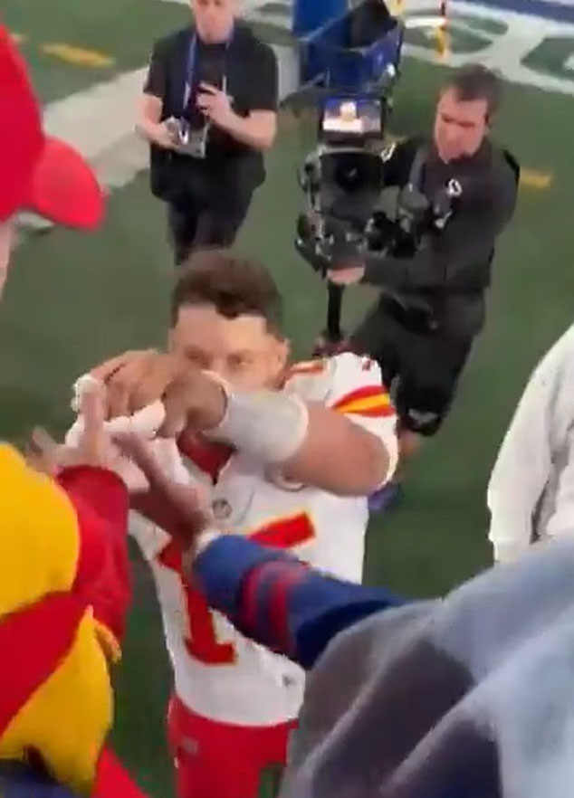 Patrick Mahomes in a white and red jersey reaching for an object from a fan.