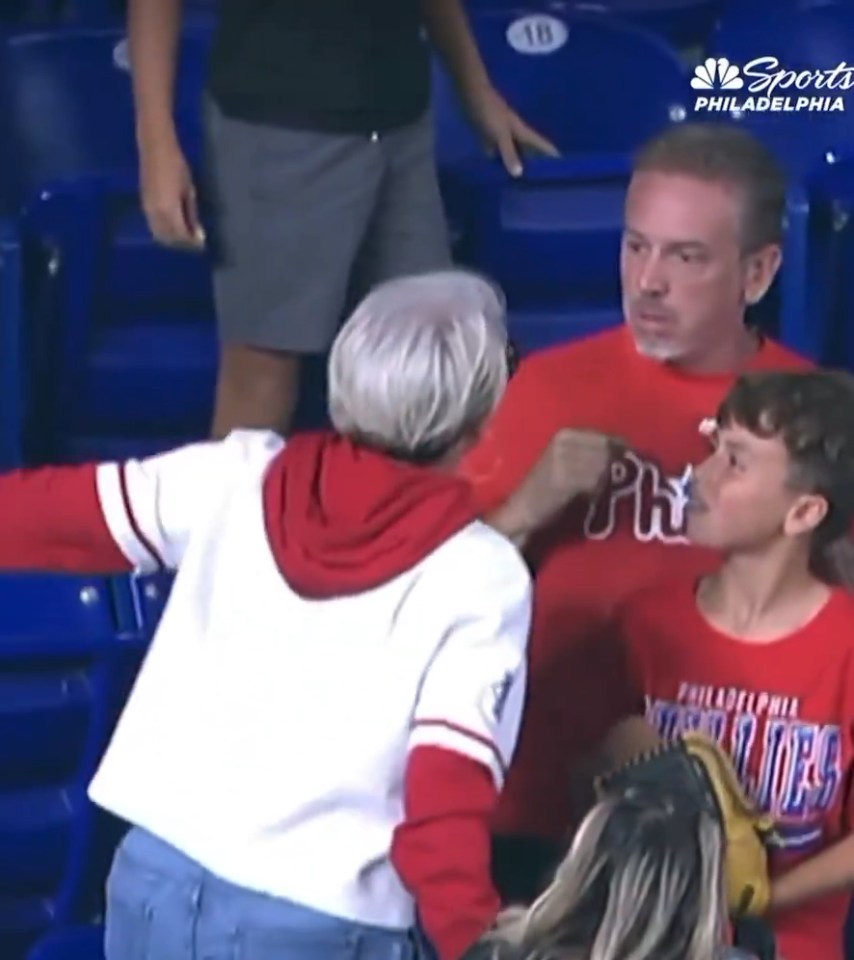 Woman in white shirt and red hoodie arguing with a man in a red Phillies shirt, next to a boy in a red shirt.