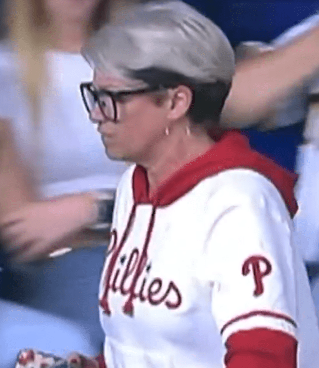 A woman in glasses and a Phillies hoodie walks past a man.