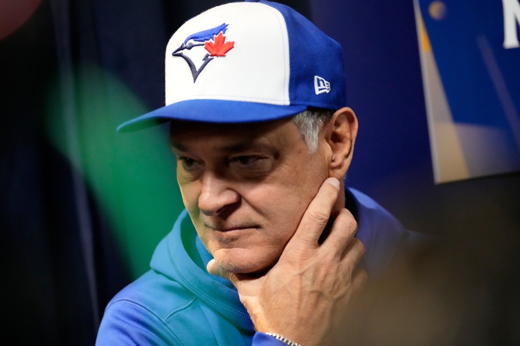 Don Mattingly wearing a blue and white Toronto Blue Jays baseball cap, holding his chin.