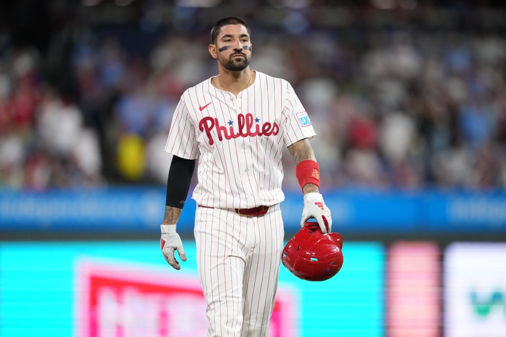 Philadelphia Phillies baseball player wearing a white pinstripe jersey with "Phillies" in red script, black eye black, and holding a red helmet.